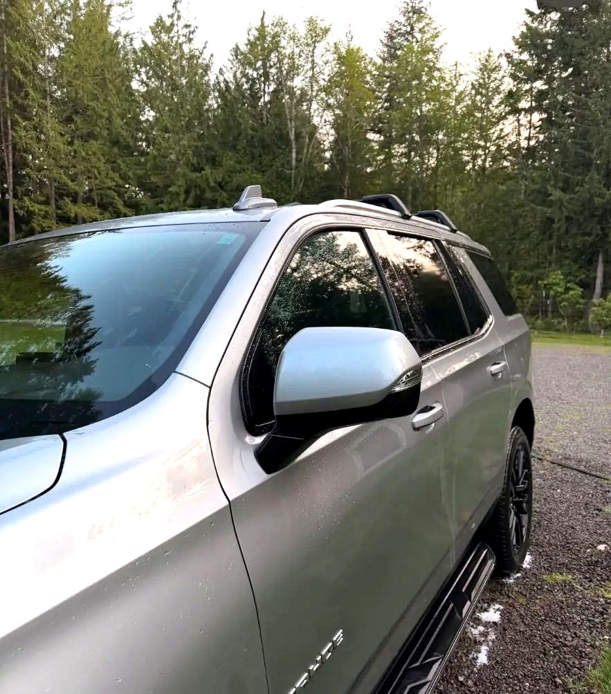 Side profile of a clean silver Chevy Tahoe with trees reflecting in the windows